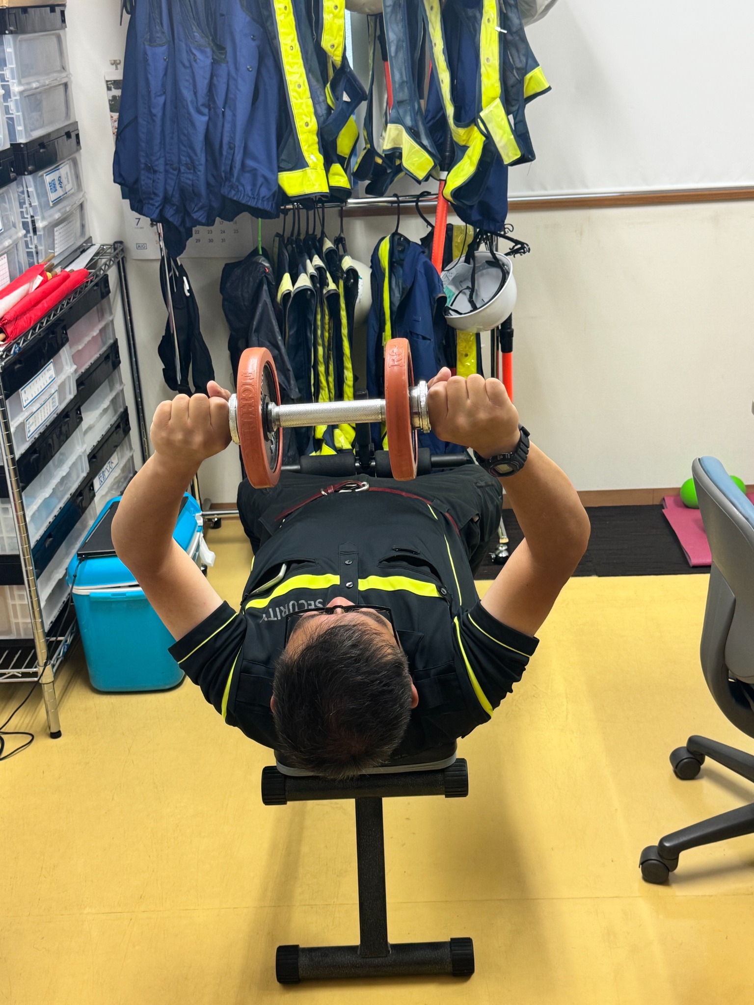 事務所のトレーニングベンチで筋力トレーニングをする社員